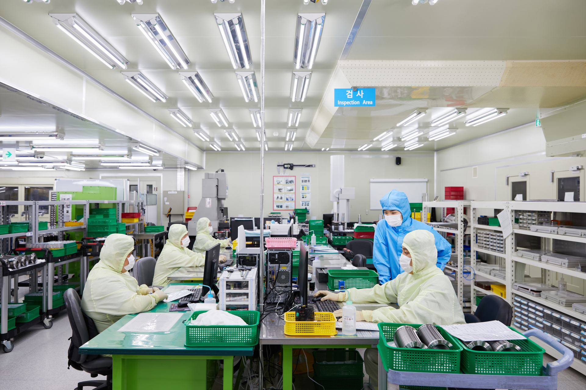 Two Employees in Dark Blue Clean Room Gown with another KSM employee in Green gown in manufacturing room background.